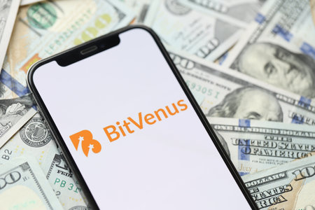 KYIV, UKRAINE - MARCH 15, 2024 Bitvenus logo on iPhone display screen with many hundred dollar bills. Cryptocurrency exchange portalのeditorial素材