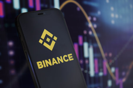 KYIV, UKRAINE - MARCH 15, 2024 Binance logo on iPhone display screen and crypto currency value charts. Cryptocurrency exchange portalのeditorial素材