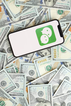 KYIV, UKRAINE - APRIL 1, 2024 Wechat or Weixin icon on smartphone screen and many usd money bills....