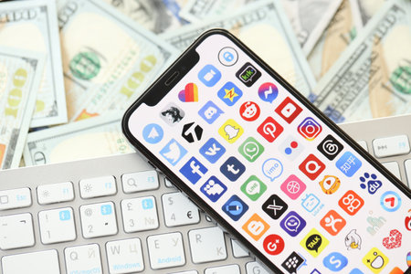 KYIV, UKRAINE - APRIL 1, 2024 Many apps icon on smartphone screen on many usd money bills. iPhone...