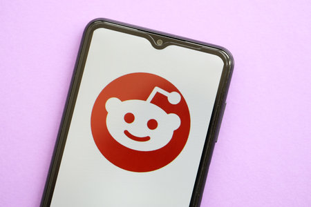 KYIV, UKRAINE - APRIL 1, 2024 Reddit icon on smartphone screen on purple table close up. iPhone display with app logo on lilac backgroundのeditorial素材
