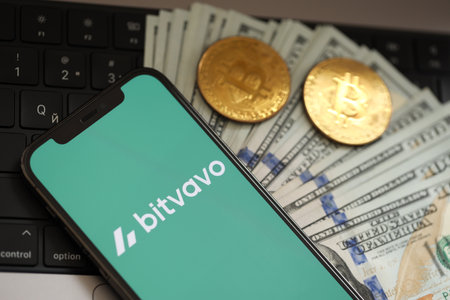 KYIV, UKRAINE - MARCH 15, 2024 Bitvavo logo on iPhone display screen with dollars and bitcoins on MacBook. Cryptocurrency exchange portalのeditorial素材