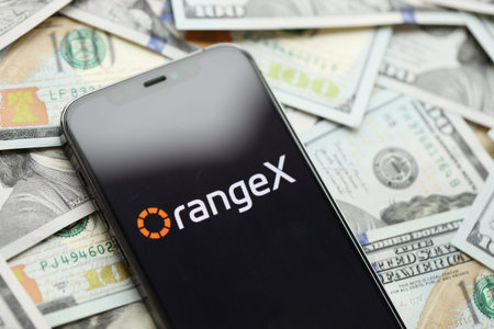 KYIV, UKRAINE - MARCH 15, 2024 OrangeX logo on iPhone display screen with many hundred dollar bills. Cryptocurrency exchange portalのeditorial素材