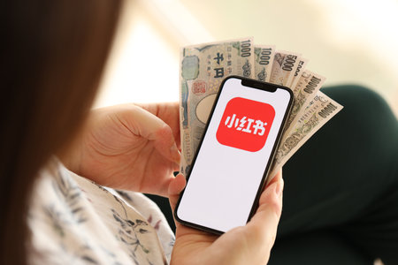 KYIV, UKRAINE - APRIL 1, 2024 Xiaohongshu icon on smartphone screen and money in female hand. iPhone display with app logo and japanese yen money bills in women hands close upのeditorial素材
