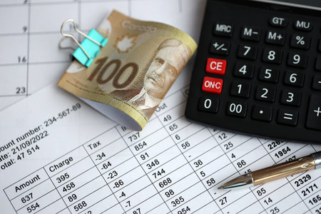 Many calculation results in schedules lies on table with Canadian money bills, calculator and pen close up. Taxation and annual accountant paperwork in Canadaの写真素材
