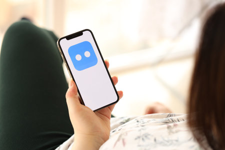KYIV, UKRAINE - APRIL 1, 2024 Botim messenger icon on smartphone screen in young female hands indoors. Woman using iPhone app at homeのeditorial素材