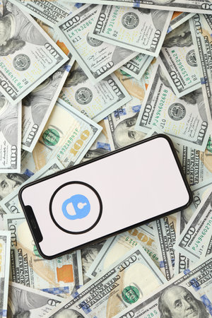 KYIV, UKRAINE - APRIL 1, 2024 OnlyFans icon on smartphone screen and many usd money bills. iPhone display with app logo and lot of hundred dollars banknotes close upのeditorial素材