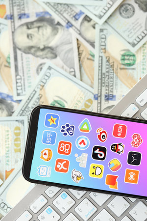 KYIV, UKRAINE - APRIL 1, 2024 Asian apps icon on smartphone screen on many usd money bills. iPhone display with app logo and dollar banknotes with white keyboardのeditorial素材