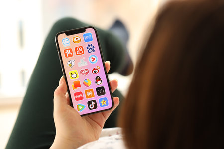 KYIV, UKRAINE - APRIL 1, 2024 Asian apps icon on smartphone screen in young female hands indoors. Woman using iPhone app at homeのeditorial素材