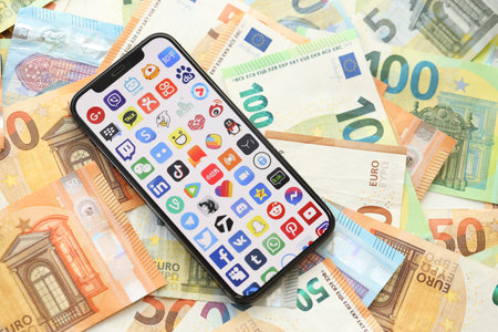 KYIV, UKRAINE - APRIL 1, 2024 Many apps icon on smartphone screen on many euro money bills. iPhone display with app logo with european currency euro banknotesのeditorial素材