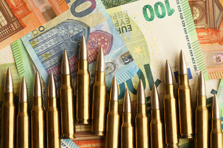 Yellow cartridges and shell casings on euro banknotes. Lot of bills of European union currency and ammo close upの写真素材