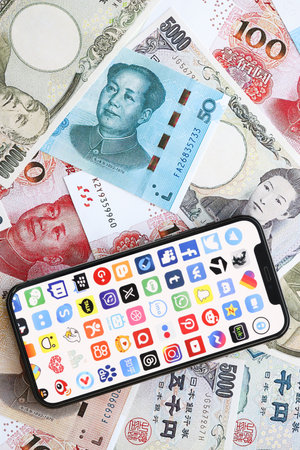 KYIV, UKRAINE - APRIL 1, 2024 Many apps icon on smartphone screen on many asian money bills. iPhone display with app logo with japanese yen and chinese yuan banknotesのeditorial素材