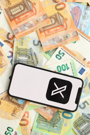 KYIV, UKRAINE - APRIL 1, 2024 Twitter X icon on smartphone screen on many euro money bills. iPhone display with app logo with european currency euro banknotesのeditorial素材