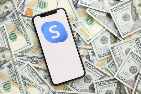 KYIV, UKRAINE - APRIL 1, 2024 Skype icon on smartphone screen and many usd money bills. iPhone display with app logo and lot of hundred dollars banknotes close upのeditorial素材