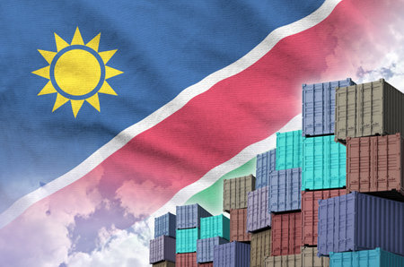 Namibia flag and big stack of shipping cargo containers in docks with sky background close upの写真素材
