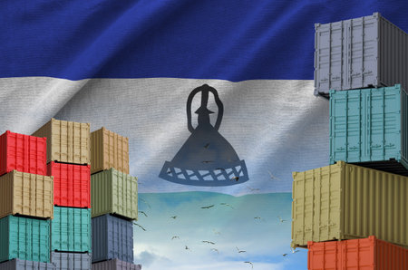 Lesotho flag and big stack of shipping cargo containers in docks with sky background close upの写真素材