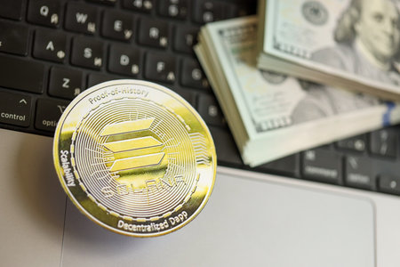KYIV, UKRAINE - AUGUST 17, 2024 Solana SOL coin with big amount of hundred US dollar bills on laptop...