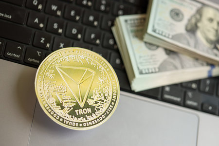 KYIV, UKRAINE - AUGUST 17, 2024 TRON Coin with big amount of hundred US dollar bills on laptop surface close upのeditorial素材