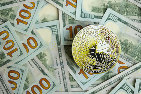 KYIV, UKRAINE - AUGUST 17, 2024 Ripple XRP Coin on big amount of hundred US dollar bills close upのeditorial素材