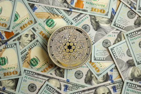 KYIV, UKRAINE - AUGUST 17, 2024 Cardano ADA coin on big amount of hundred US dollar bills close upのeditorial素材