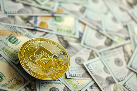 KYIV, UKRAINE - AUGUST 17, 2024 Binance BNB coin on big amount of hundred US dollar bills close upのeditorial素材