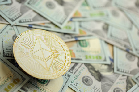 KYIV, UKRAINE - AUGUST 17, 2024 Ethereum ETH coin on big amount of hundred US dollar bills close upのeditorial素材
