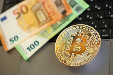 KYIV, UKRAINE - AUGUST 17, 2024 Bitcoin BTC coin with big amount of european euro bills on laptop surface close upのeditorial素材