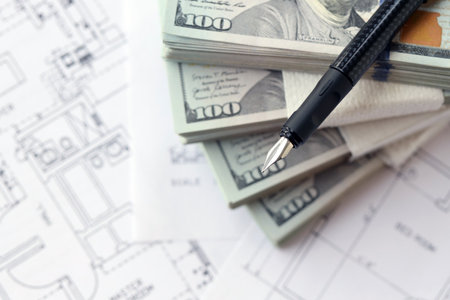 Big amount of US dollars money bills with pen and planning blueprints of residential building project close up. Investment and construction project conceptの写真素材
