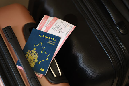 Canadian passport with tickets lies on touristic suitcase close up in airport waiting hall. Travel worldwide and international tourism conceptの写真素材