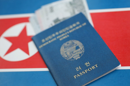 North Korean won money bills in big amount and passport lies on People Republic of Korea flag close up. Finance and banking conceptの写真素材
