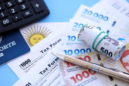 Argentine pesos money bills in big amount lies on table with pen, calculator, passport and tax forms close up. Finance and banking conceptの写真素材