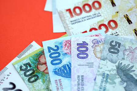 Argentine pesos money bills in big amount lies on red color table close up. Finance and banking conceptの写真素材