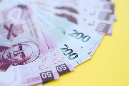Mexican pesos money bills in big amount lies on yellow color table close up. Finance and banking...