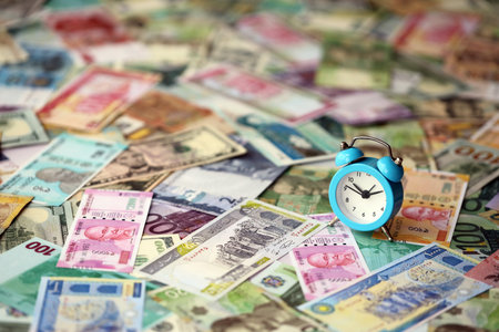 Small alarm clock on many banknotes of different currency. Background of time and money close upの写真素材