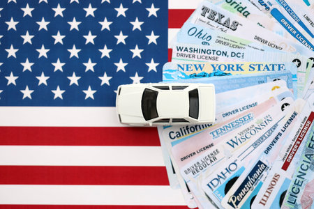 Toy car on big amount of driving licenses from different USA states on flag close up. Stack of...