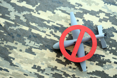 Unnamed grey toy drone model and red prohibition sign on camouflage fabric close up. Anti-aircraft...