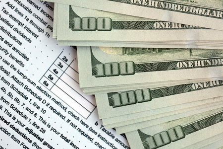 Big amount of United States hundred dollar bills in bunch on table with individual income tax return...
