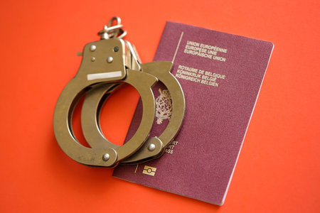 Belgium passport with police handcuffs on table close up.の写真素材