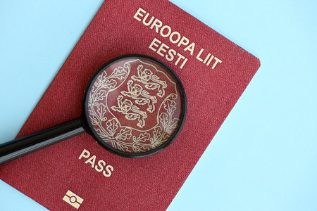 Estonia passport and magnifying glass on light blue paper background close up. Citizenship details and information conceptの写真素材