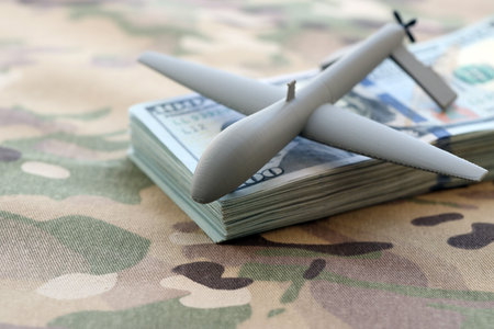 Unnamed grey toy drone model and dollar bills on camouflage fabric close up.の写真素材
