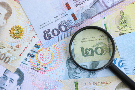 Thai baht currency money bills and magnifying glass close up. The concept of financial monitoring and taxationの写真素材