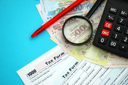 Vietnamese dong money bills and calculator with tax form close up on blue. Taxation and accounting conceptの写真素材