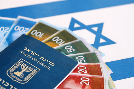 Israel New Shekels banknotes and passport on flag. The current Israel money bills and biometrical pass lies on flag in big amount. The concept of travel and vacation in Israelの写真素材