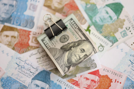 Roll of US dollar bills lies on big amount of Pakistan rupees banknotes close up. American money bunch lies on Pakistan money bills. The concept of economics and currency exchange in Pakistanの写真素材