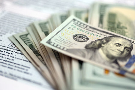Big amount of United States USD dollar bills on table with 1040 individual income tax return form....