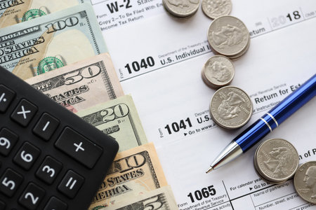 American US dollars money bills and coins with pen and calculator on IRS tax form blanks close up....