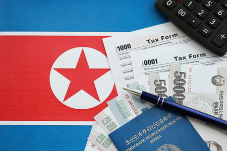 North Korean won money bills in big amount lies on table with pen, calculator, passport and tax forms close up. Taxpaying and accounting conceptの写真素材