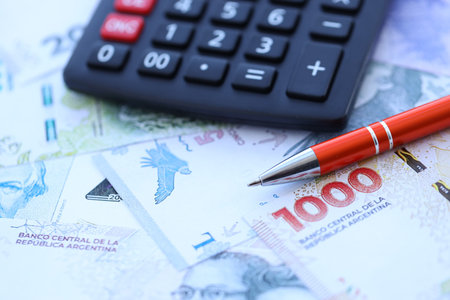 Argentine pesos money bills in big amount lies on table with pen and calculator close up. Finance and tax paying conceptの写真素材