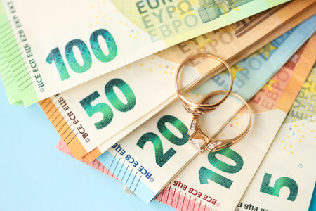 European union Euro money bills and coins with wedding rings on blue table close upの写真素材