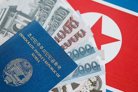 North Korean won money bills in big amount and passport lies on People Republic of Korea flag close...